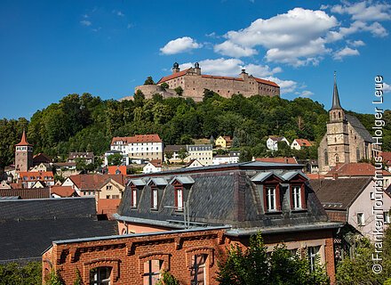 Blick über eine Kleinstadtkulisse hinauf zu einer mächtigen Burganlage