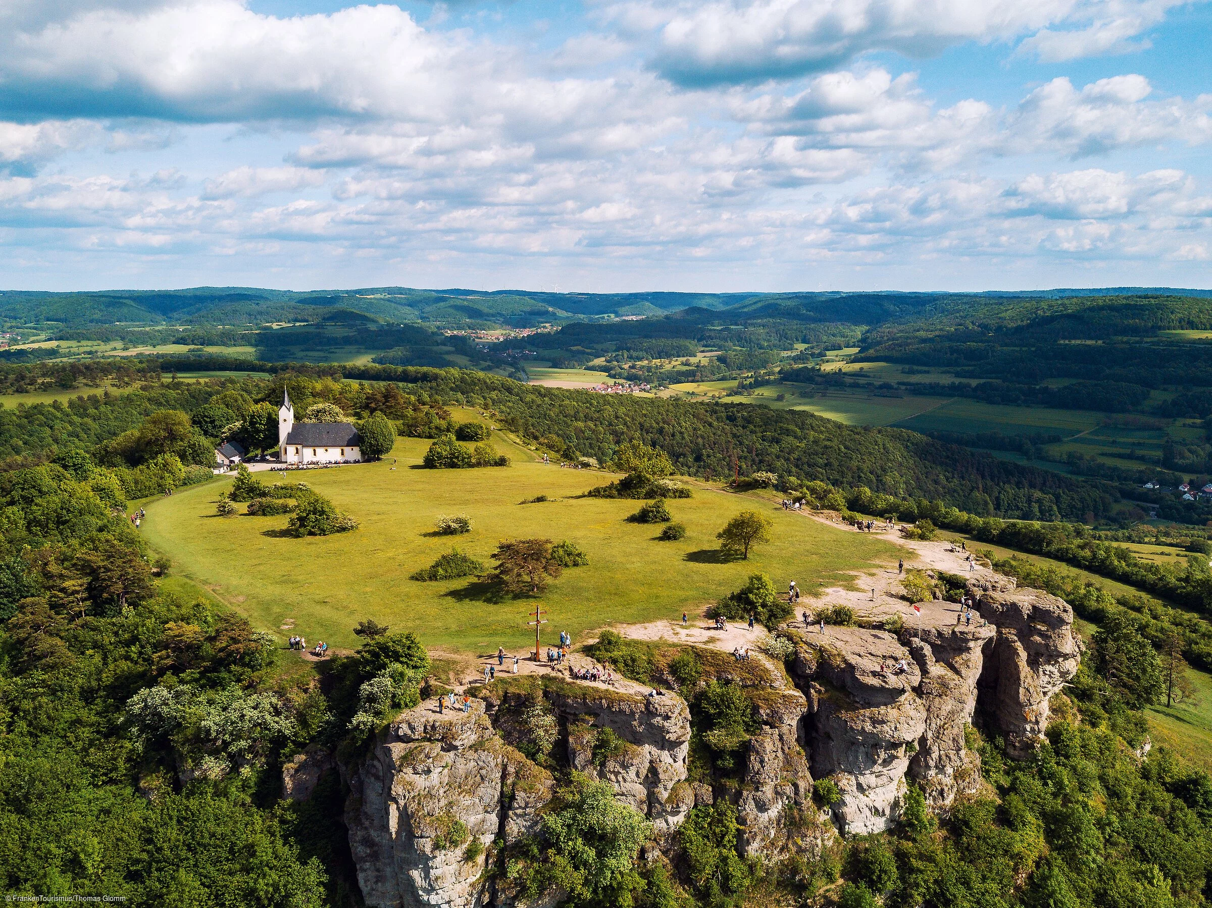 Ein Hochplateau mit einem kleinen Kirchlein inmitten von grünen Wiesen und Bäumen.