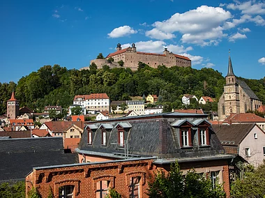 Blick über eine Kleinstadtkulisse hinauf zu einer mächtigen Burganlage