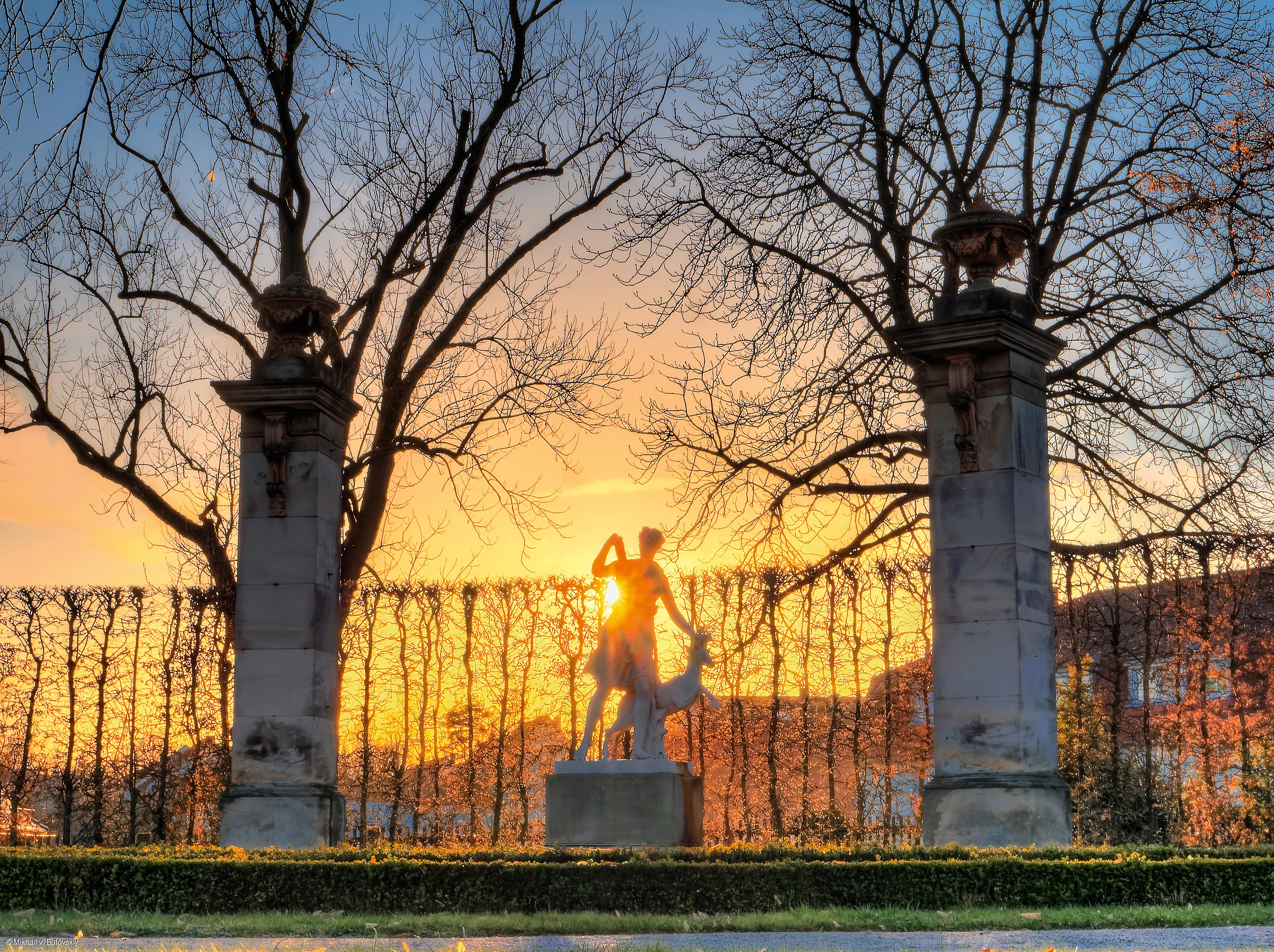 Zwischen zwei Bäumen steht eine Statue vor einem Park im Sonnenuntergang