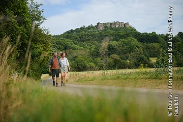 Ein Paar spaziert auf einem Weg durch eine grüne Landschaft mit Hügeln im Hintergrund.
