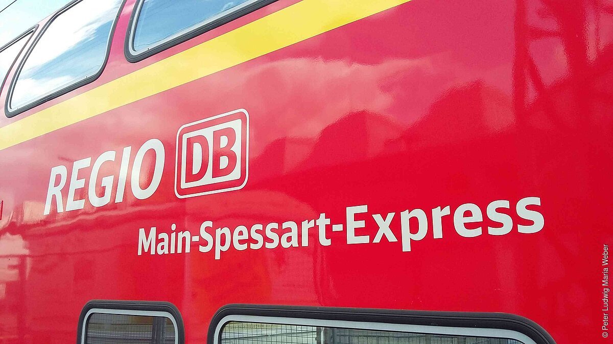 Seitenansicht eines roten Zuges mit der Aufschrift „Regio DB Main-Spessart-Express“ und gelbem Streifen oberhalb.